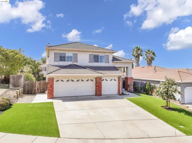 Two-story residence featuring a tile roof, brick accents, dual garage doors, a concrete driveway, and artificial turf landscaping
