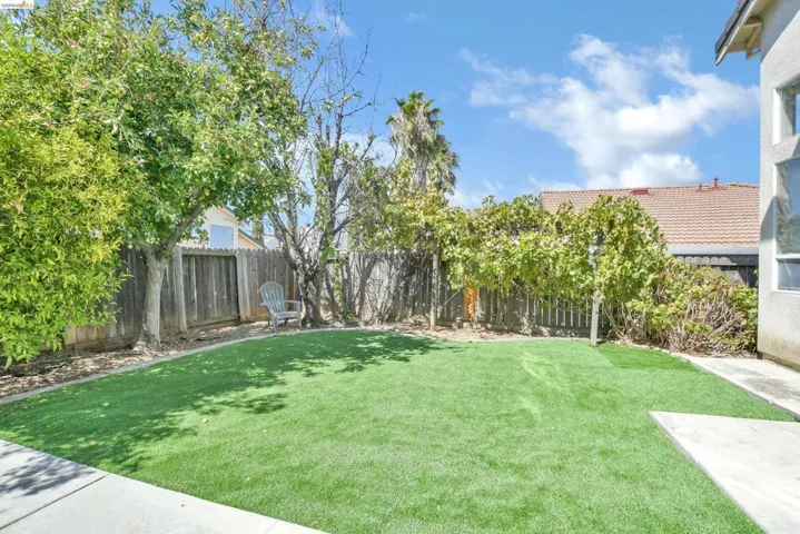 Expansive backyard featuring artificial turf, mature trees, a privacy fence, and a concrete patio area