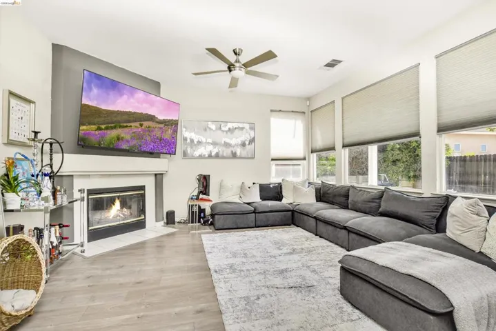 Living area featuring wood-finish flooring, a white fireplace with a dark insert, and a ceiling fan