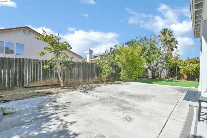 Expansive concrete patio with a partial artificial turf area, surrounded by a wooden privacy fence and mature trees