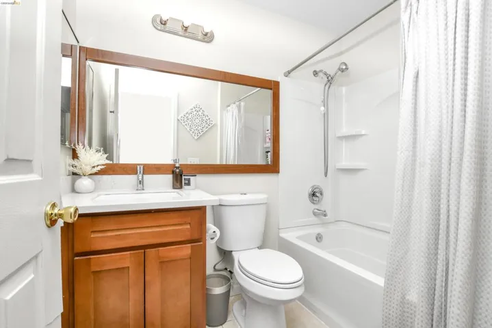 Bathroom featuring a wood-finish vanity with an integrated sink, a large framed mirror, a three-light vanity fixture, and a white tub and shower combination with chrome fixtures