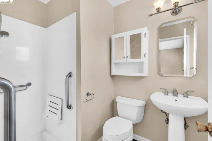 Bathroom featuring a white pedestal sink with dual-handle faucet, a beveled mirror, and a wall-mounted medicine cabinet with frosted glass panels