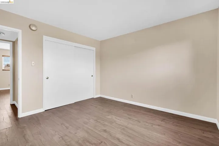 Room featuring wood-finish flooring, neutral wall paint, white baseboards, and a closet with sliding doors