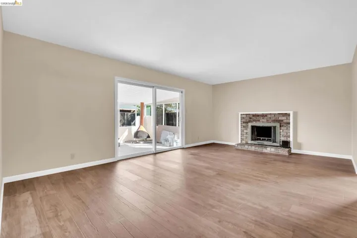 Spacious interior with wood-finish flooring, a brick fireplace, and sliding glass doors opening to an outdoor patio with a covered section