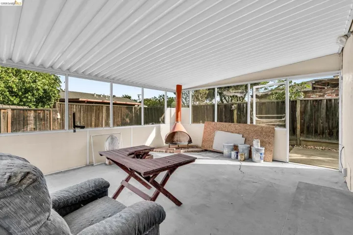Enclosed patio featuring a corrugated overhead cover, a free-standing fireplace, concrete flooring, and perimeter windows
