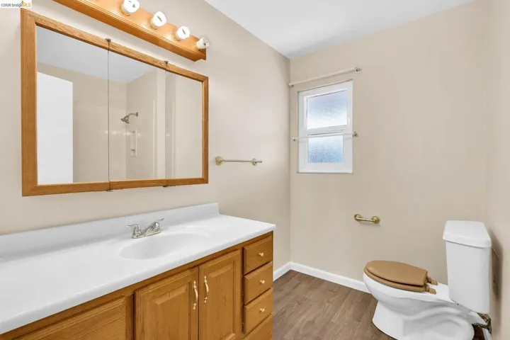 Bathroom featuring a wood-finish vanity with a white countertop and integrated sink, a large mirrored medicine cabinet, and a white toilet