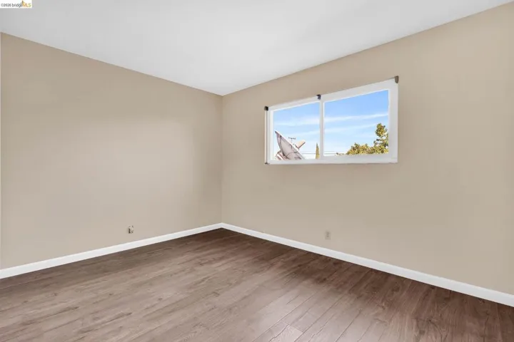 Room featuring wood-finish flooring, neutral wall paint, white trim, and a white-framed window