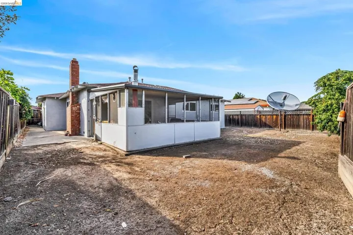 Rear exterior featuring a brick chimney, enclosed patio, and a concrete side path