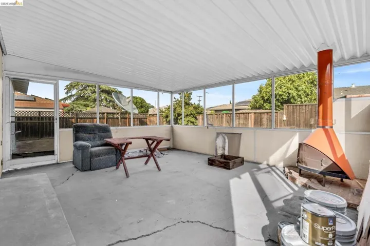 Screened-in patio space featuring a corrugated metal roof, concrete flooring, and an orange freestanding fireplace