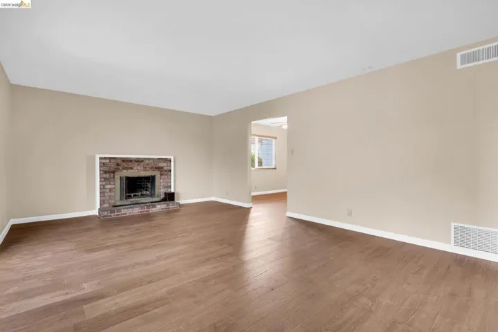 Spacious living area featuring wood-finish flooring, a brick fireplace with a hearth, light neutral wall tones, and white baseboards