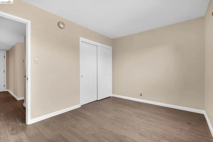 Room featuring wood-finish flooring, neutral wall paint, white baseboards, and white sliding closet doors