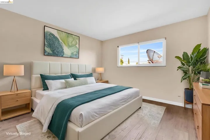 Spacious room featuring wood-finish flooring, a large window, light-toned walls, and white baseboards