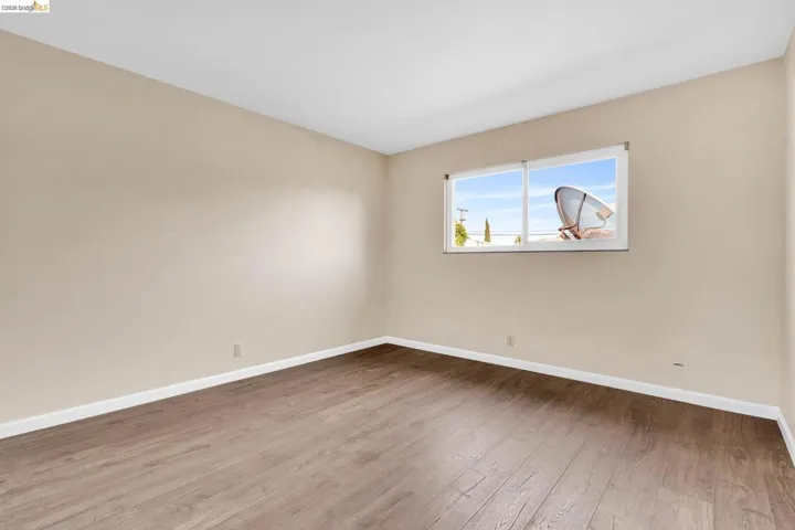 Light-filled room featuring wood-finish flooring, neutral wall tones, white baseboards, and a large window with white framing