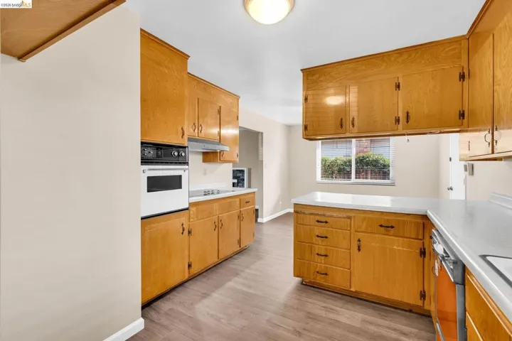 Kitchen featuring wood-finish cabinetry, white countertops, built-in oven, and wood-finish flooring