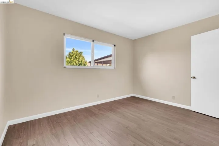 Windowed interior space with wood-finish flooring, white baseboards, and neutral wall tones