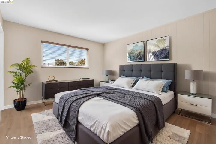 Spacious bedroom featuring wood-finish flooring, a wide window with blinds, and neutral wall tones
