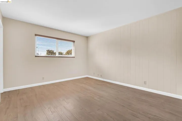 Spacious room featuring wood-finish flooring, a window with blinds, and paneling on one wall