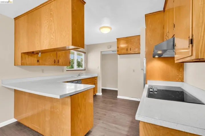 Kitchen featuring light wood cabinetry, stone-finish countertops, wood-finish flooring, a built-in electric cooktop, and a stainless steel range hood