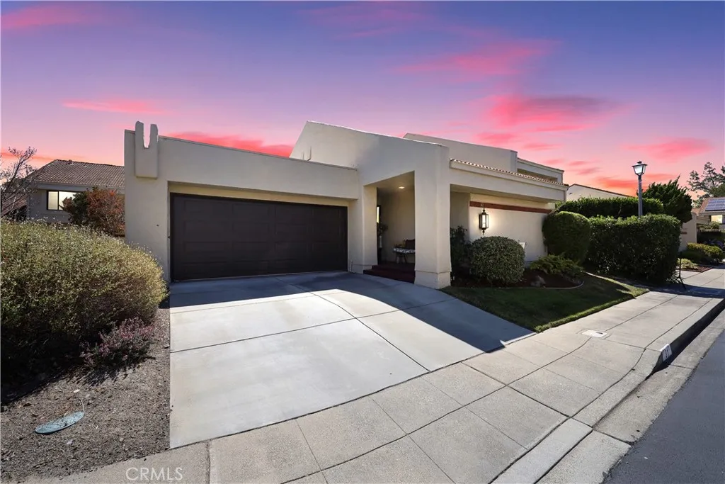 Attractive front exterior with a two-car garage, low-maintenance landscaping, and excellent curb appeal highlighted by a colorful virtually enhanced sunset sky.