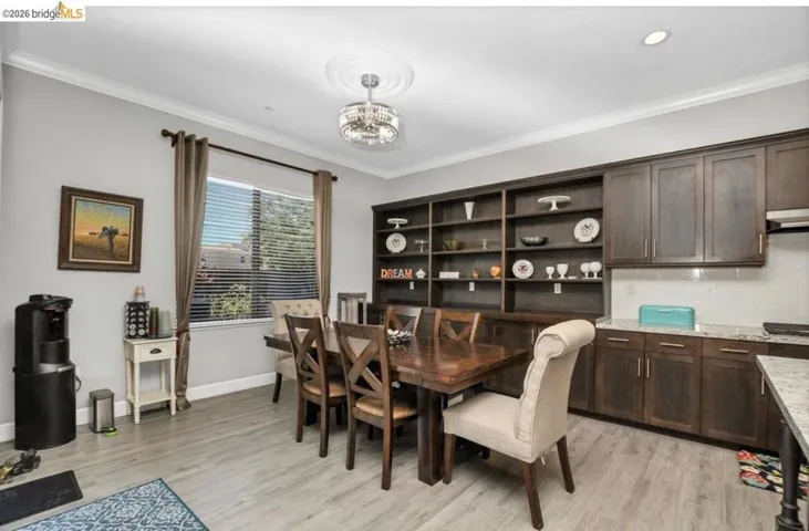 Integrated dining and kitchen space featuring wood-finish flooring, a contemporary chandelier, built-in shelving, dark wood cabinetry, and light-colored countertops