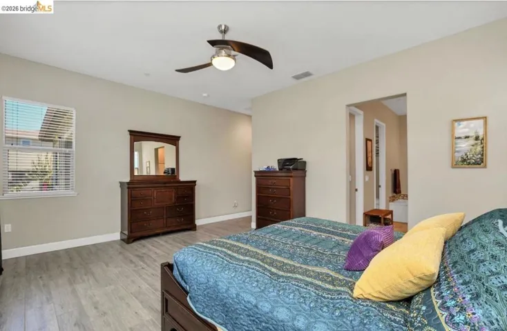 Spacious room featuring wood-finish flooring, a ceiling fan, and abundant natural light from a large window with blinds