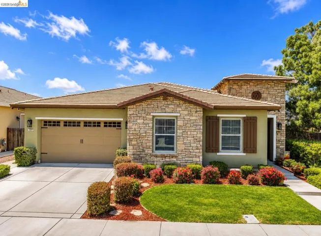 Stone and stucco exterior featuring a two-car garage, tile roof, decorative shutters, and mature landscaping