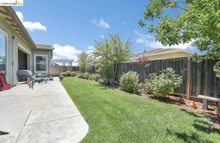 Expansive backyard featuring a concrete patio, a manicured lawn, established landscaping, and a privacy fence