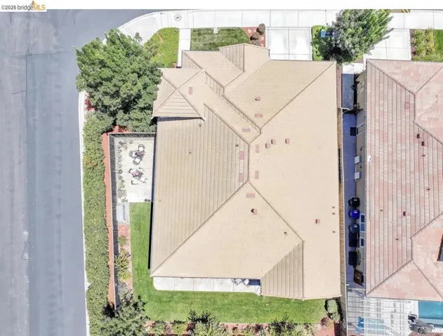 Aerial perspective showcasing a property with a tan-colored tile roof, featuring a manicured lawn, a paved patio, and mature perimeter trees