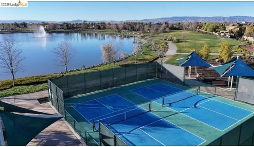Fenced outdoor courts featuring blue and green surfaces, equipped with nets and shaded seating areas