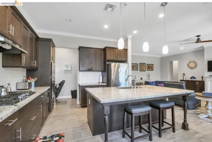 Kitchen featuring wood-finish cabinetry, stainless steel appliances, speckled stone countertops, and a central island with pendant lighting