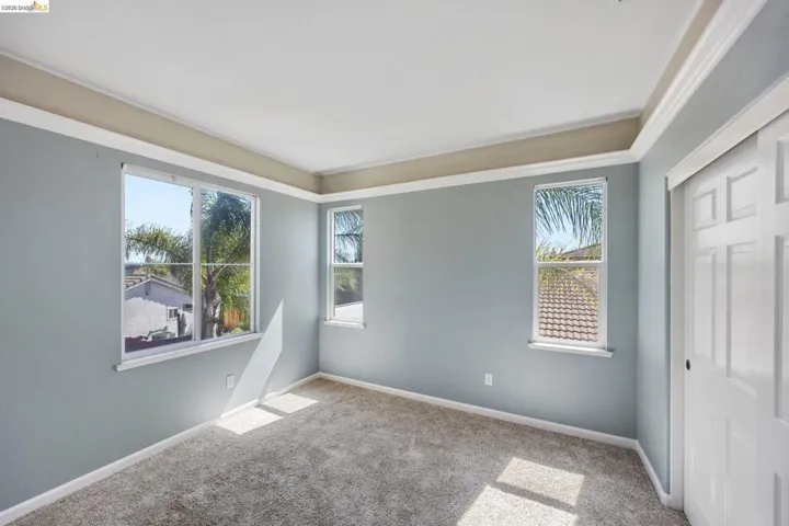 Room featuring light blue walls, gray carpet flooring, multiple white-framed windows, and a white sliding panel door