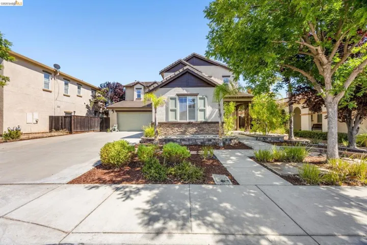Two-story stucco exterior featuring a stone facade accent, a covered entry porch, a two-car garage, and established landscaping