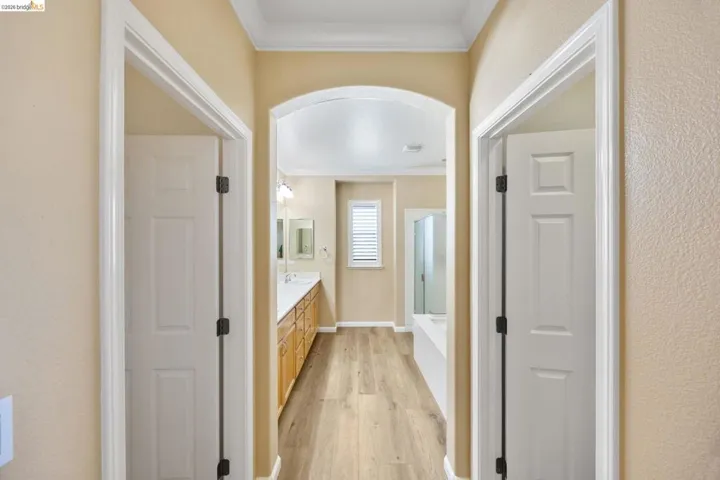 Hallway archway leading to a bathroom featuring wood-finish flooring, a double vanity with light wood cabinetry, a built-in tub, and a shower enclosure