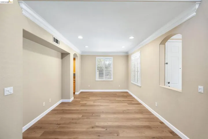 Spacious room featuring wood-finish flooring, recessed lighting, crown molding, and two windows with white plantation shutters