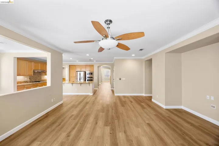 Spacious living area featuring wood-finish flooring, a ceiling fan with light fixture, and crown molding