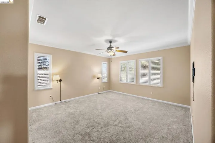 Spacious room featuring neutral carpeting, crown molding, and a ceiling fan with integrated lighting