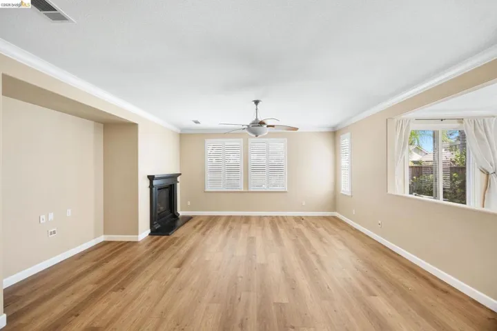 Spacious living area featuring wood-finish flooring, a decorative fireplace, ceiling fan, and multiple windows with plantation shutters