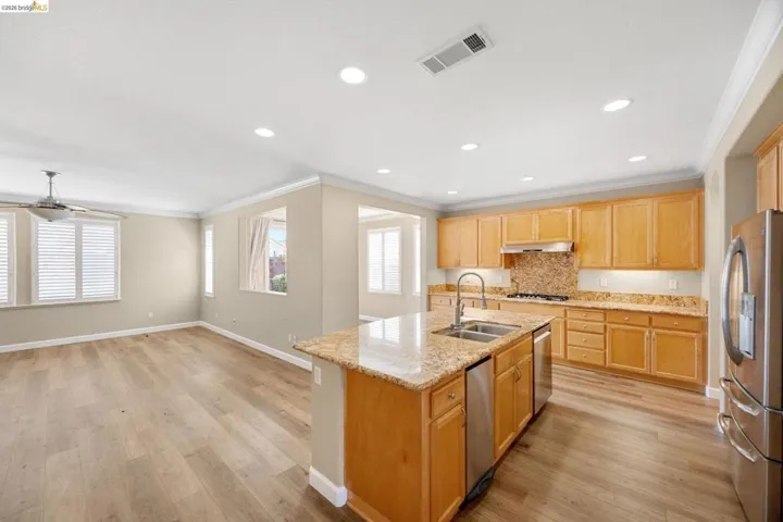 Kitchen featuring a large island with a double basin sink, stainless steel dishwasher, wood cabinetry, and granite countertops with a matching backsplash