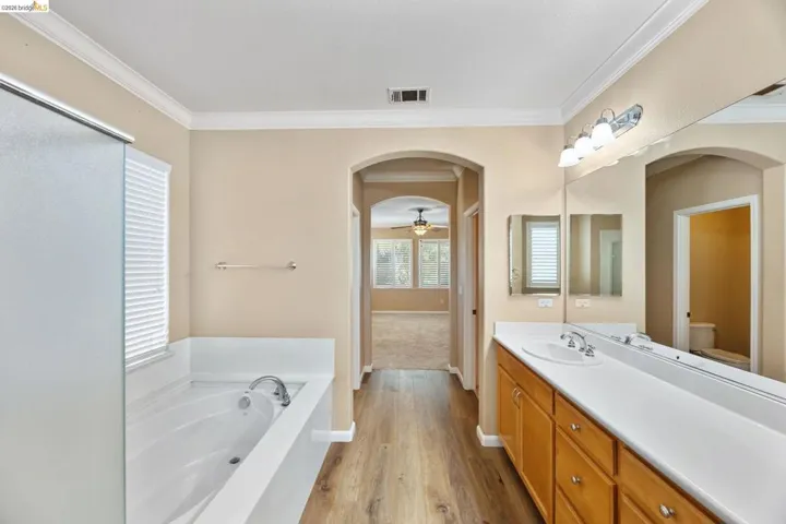 Bathroom featuring a spacious double vanity with wood cabinetry, a large mirror, and a built-in bathtub with shower enclosure
