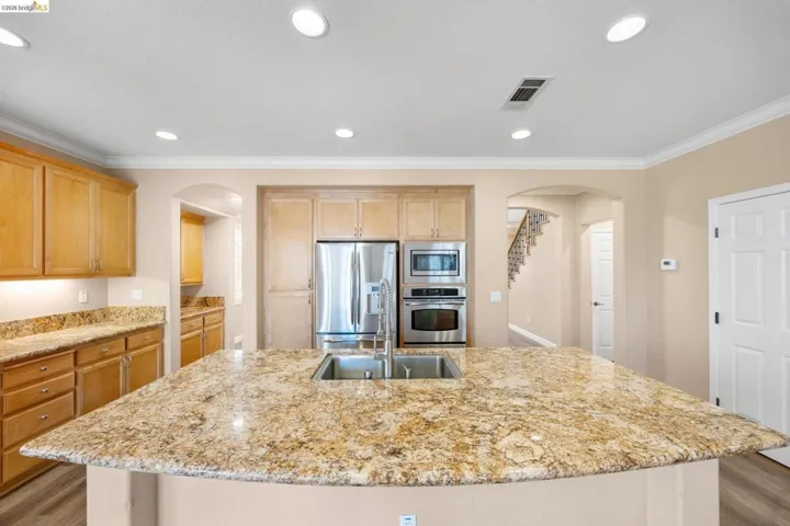 Kitchen featuring an expansive island with a double basin sink, light wood cabinetry, recessed lighting, stainless steel appliances, and wood-finish flooring