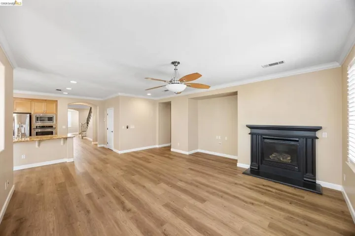 Open-concept living area featuring wood-finish flooring, a built-in fireplace with a black mantel, and a ceiling fan