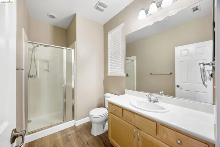 Bathroom featuring a wood-finish floor, light wood vanity with an integrated sink, large wall-mounted mirror, and a shower with a sliding glass enclosure