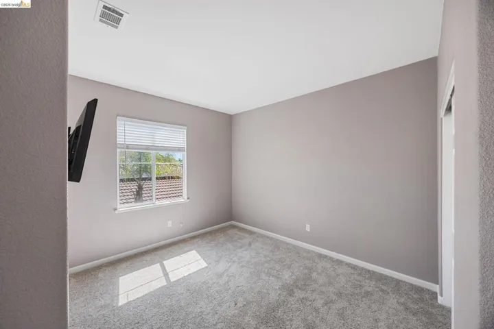 Carpeted interior room featuring a single window with blinds, light-colored wall paint, white baseboards, and a ceiling-mounted air vent