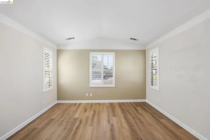 Spacious room featuring vaulted ceilings, crown molding, wood-finish flooring, and multiple windows with plantation shutters