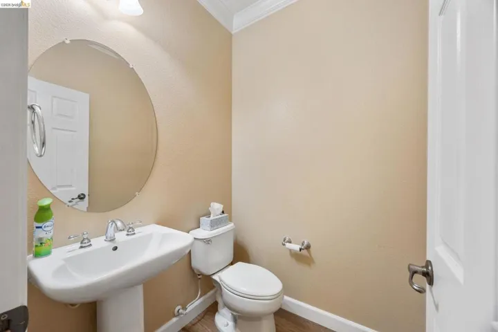 Pedestal sink with chrome fixtures, circular mirror, and overhead vanity lighting