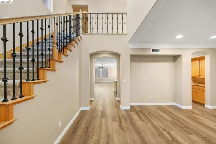 Open-concept interior featuring wood-finish flooring, a carpeted staircase with wrought iron balusters, arched doorways, and recessed lighting