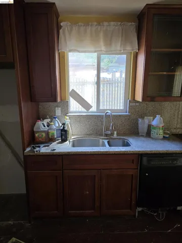 Kitchen workspace featuring a double basin stainless steel sink with a gooseneck faucet, granite-look countertops, dark wood-finish cabinetry, and a built-in black dishwasher