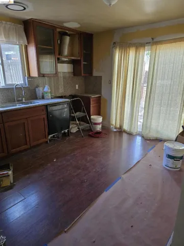 Kitchen space featuring wood-finish flooring, wood cabinetry with glass-front upper cabinets, and a stainless steel sink with a high-arc faucet
