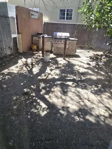 Outdoor cooking area featuring a stainless steel grill with stone-look base cabinetry and a chain-link fence