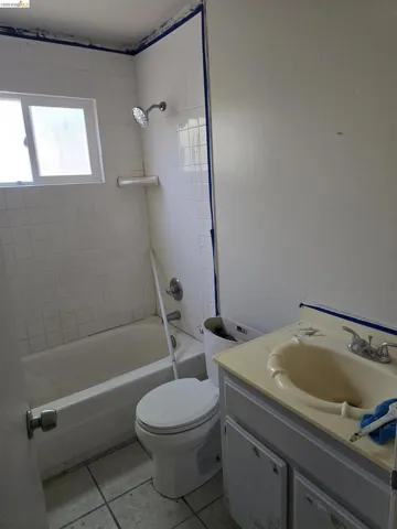 Bathroom featuring a built-in bathtub, a window, white tiled shower walls, a toilet, and a vanity with an integrated sink